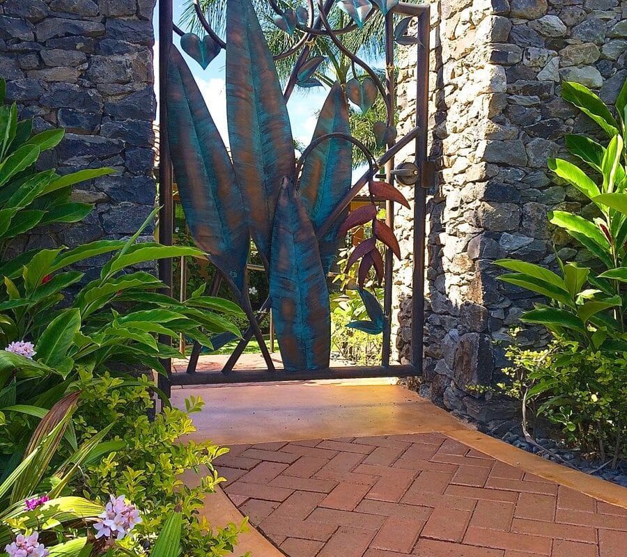 Artistic metal gate with a nature-inspired design at a stone-walled entrance.