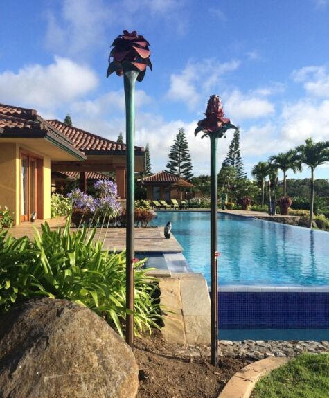 A serene poolside scene with tiki torches and tropical plants under a blue sky.