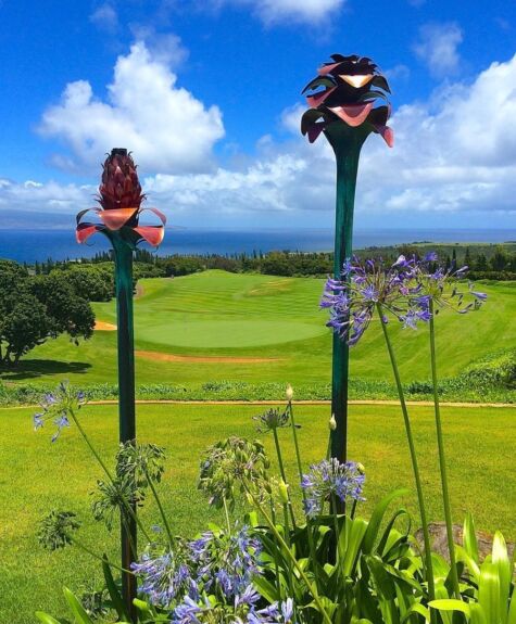 Garden with tall flower sculptures overlooking a green landscape and ocean.