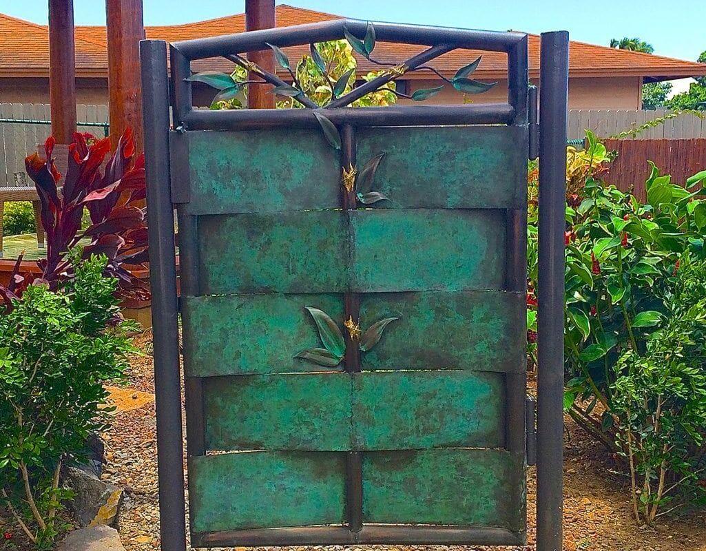 Rustic green metal gate with a patchwork design in a garden setting.