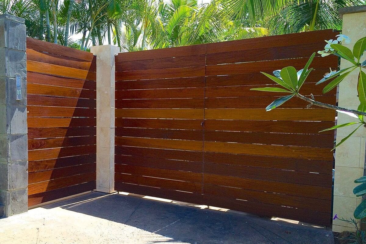 Modern wooden gate with horizontal slats in a tropical setting.
