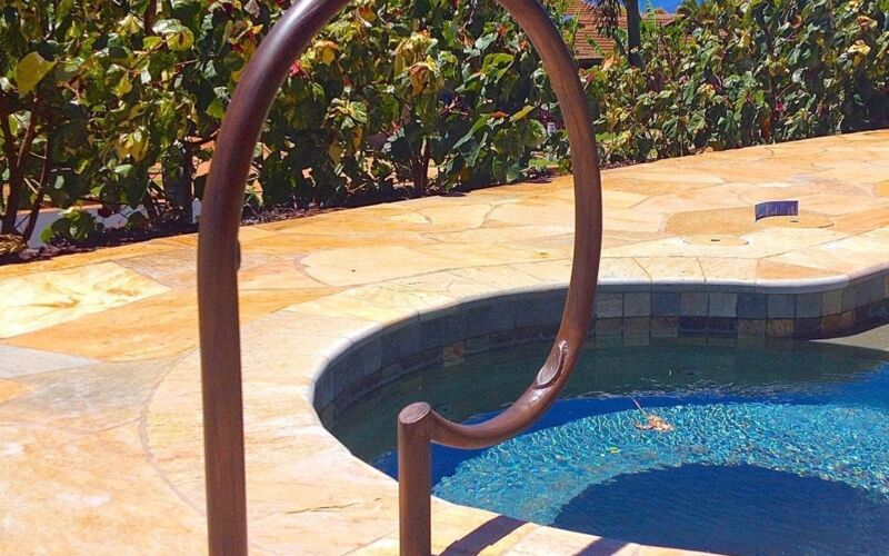 Curved handrail leading into a small pool under clear blue skies.