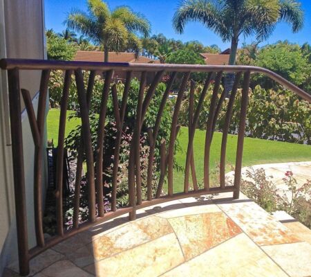 Curved balcony railing overlooking a sunny garden with palm trees.