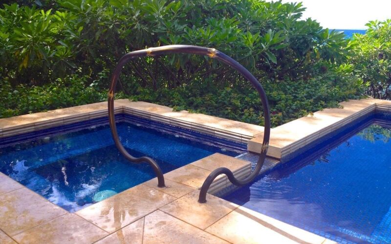 Unique pool handrails designed like swan necks beside a blue-tiled pool.
