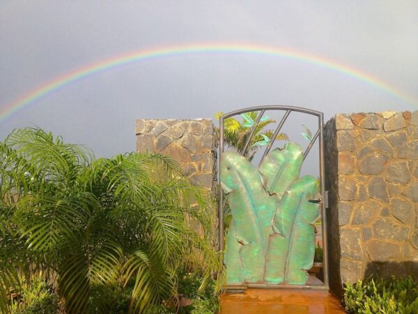 A rainbow arches over a garden with green plants and stone pillars.