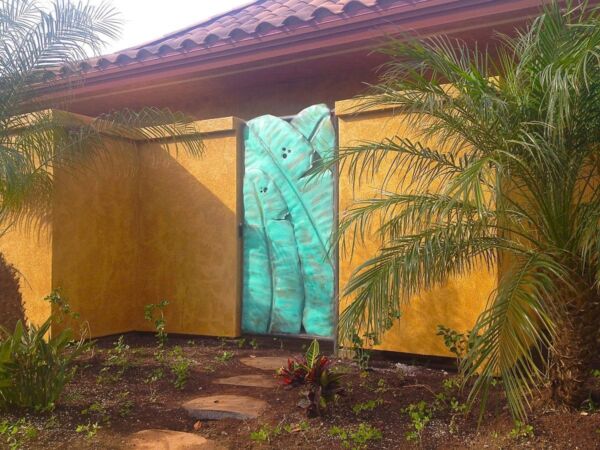 Turquoise carved wooden door in orange wall with garden plants.