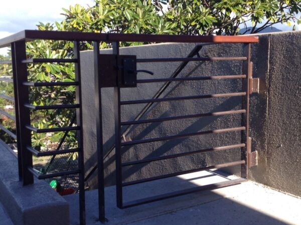 Black metal gate at the entrance of a driveway in a sunny suburban area.