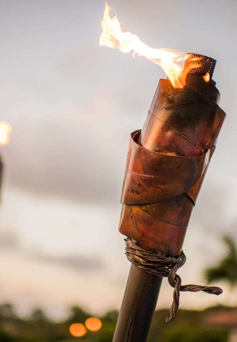 A tiki torch burning with a bright flame outdoors.