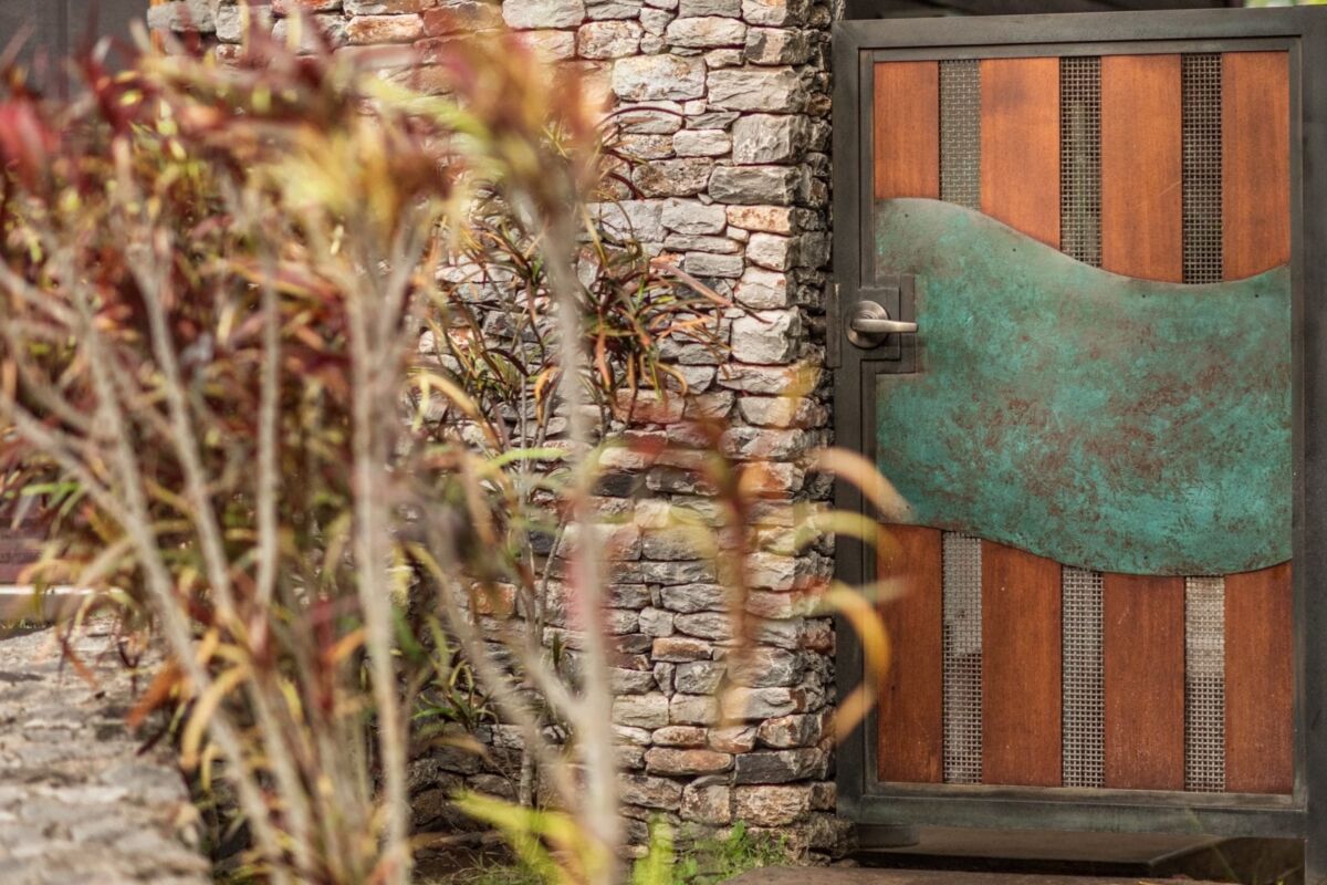 Green frog sculpture near a wooden door on a stone wall.