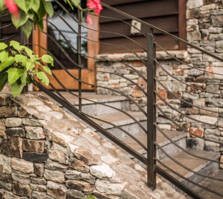 Stone stairs with a sleek black metal railing beside a wooden door.