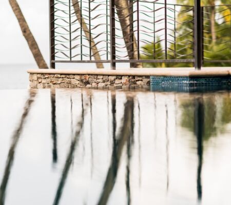 Reflections of palm trees on a calm pool surface near a stone wall.