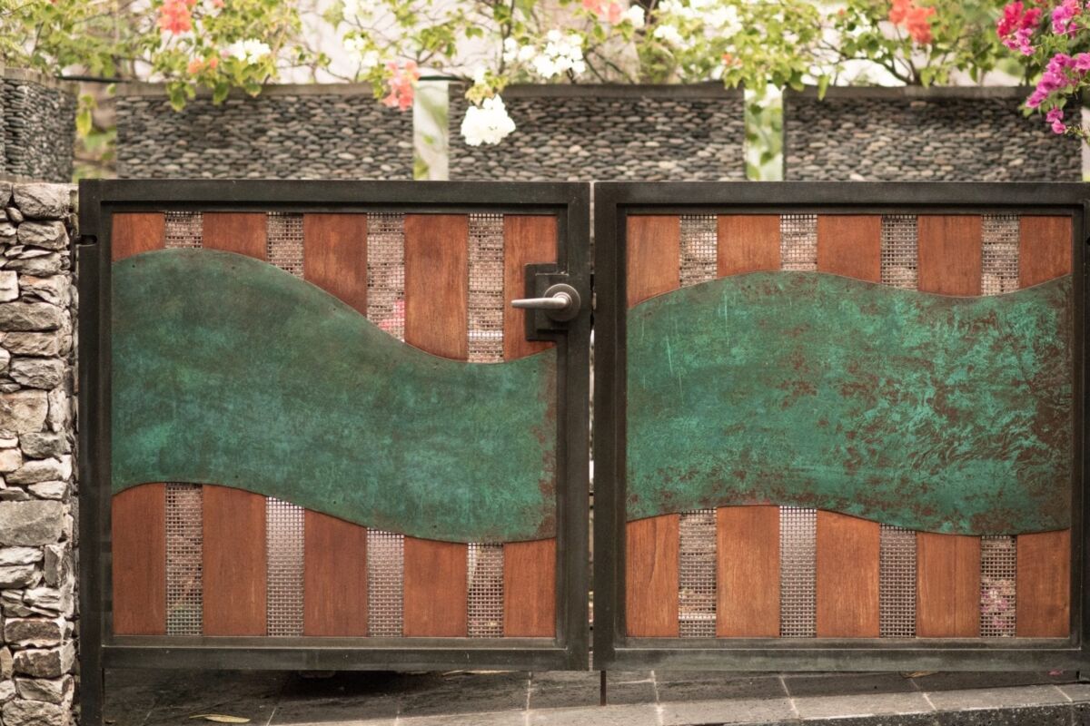 Decorative metal gate with a green wave pattern and brick wall background.