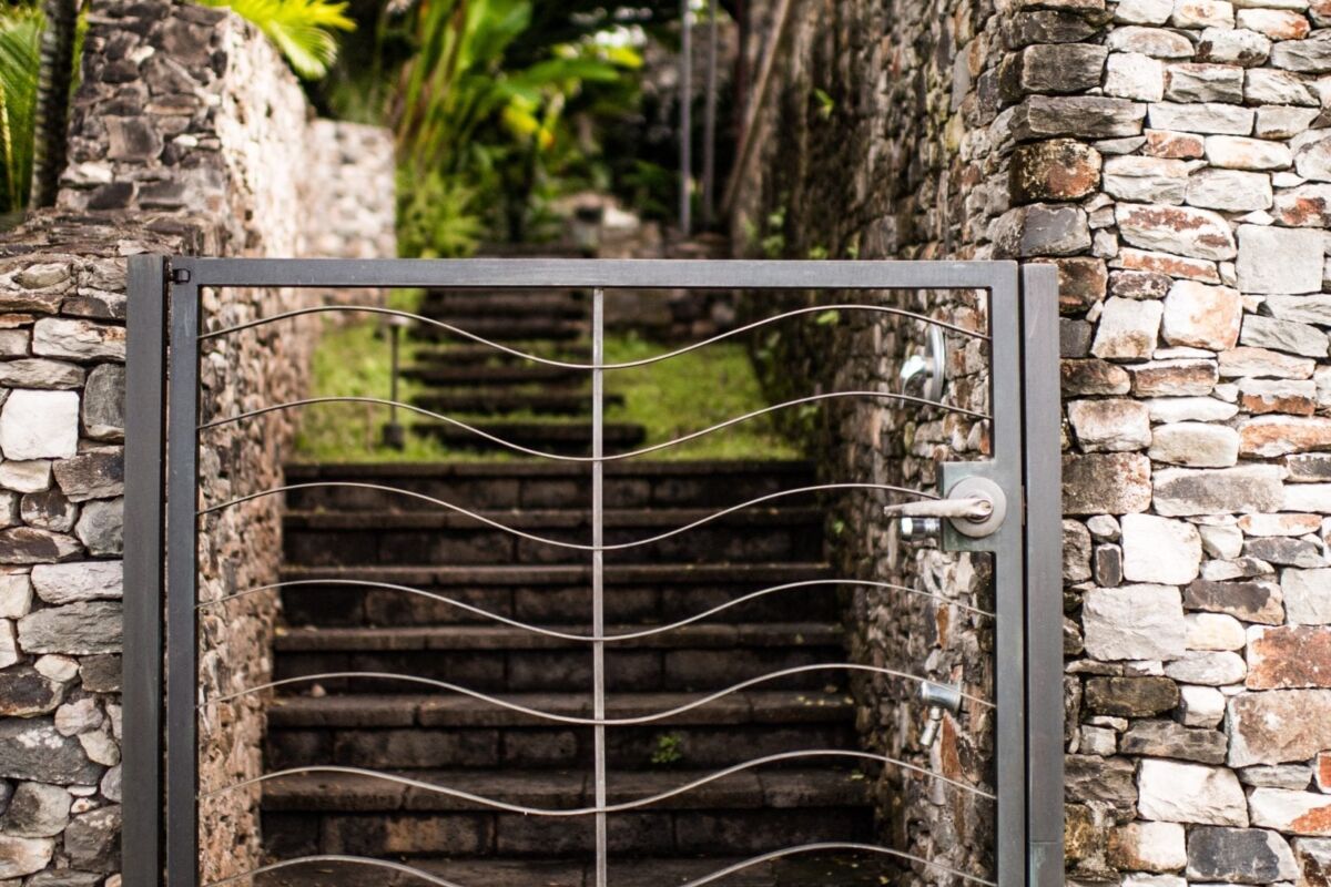 Stone staircase with metal gate surrounded by palm trees and stone walls.