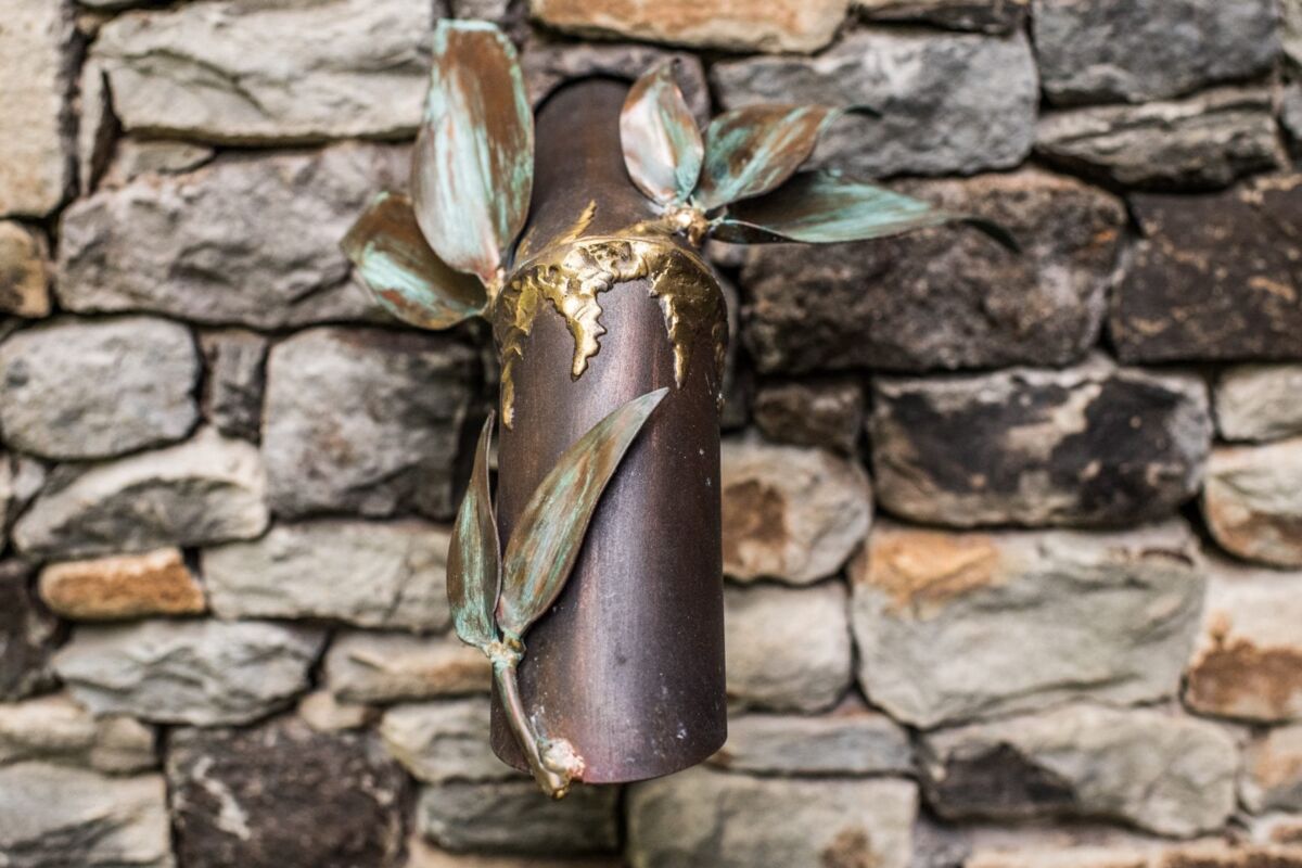 Rustic metal wall vase with leaves mounted on a stone wall.