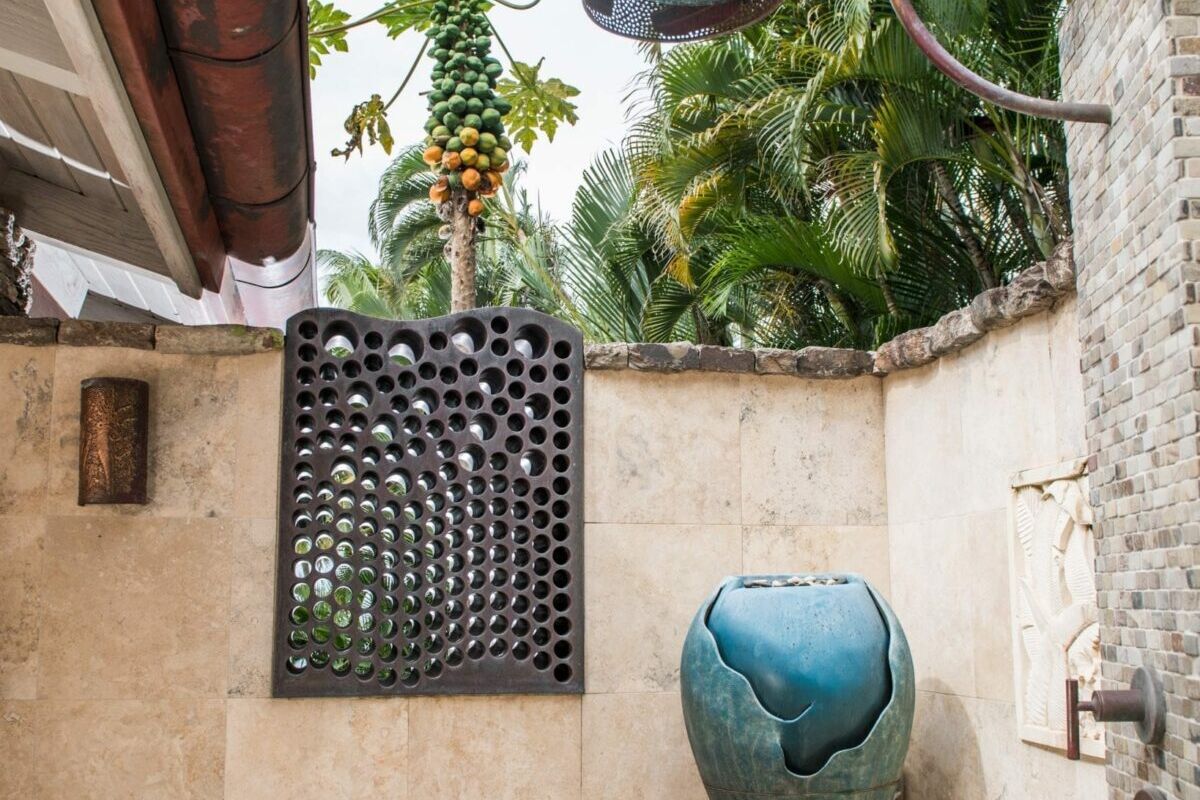 Outdoor bathroom with stone walls, a blue ceramic vase, and hanging plants.
