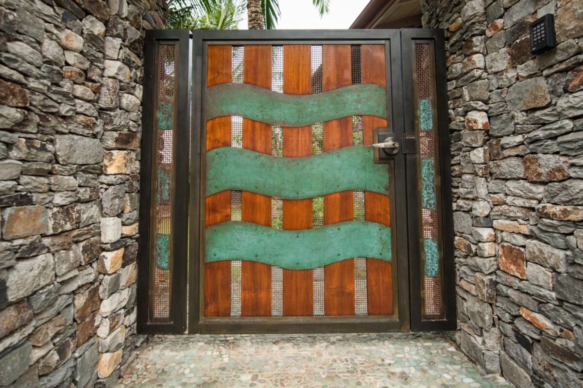 Decorative wooden gate with wavy green glass inserts and stone pillars.