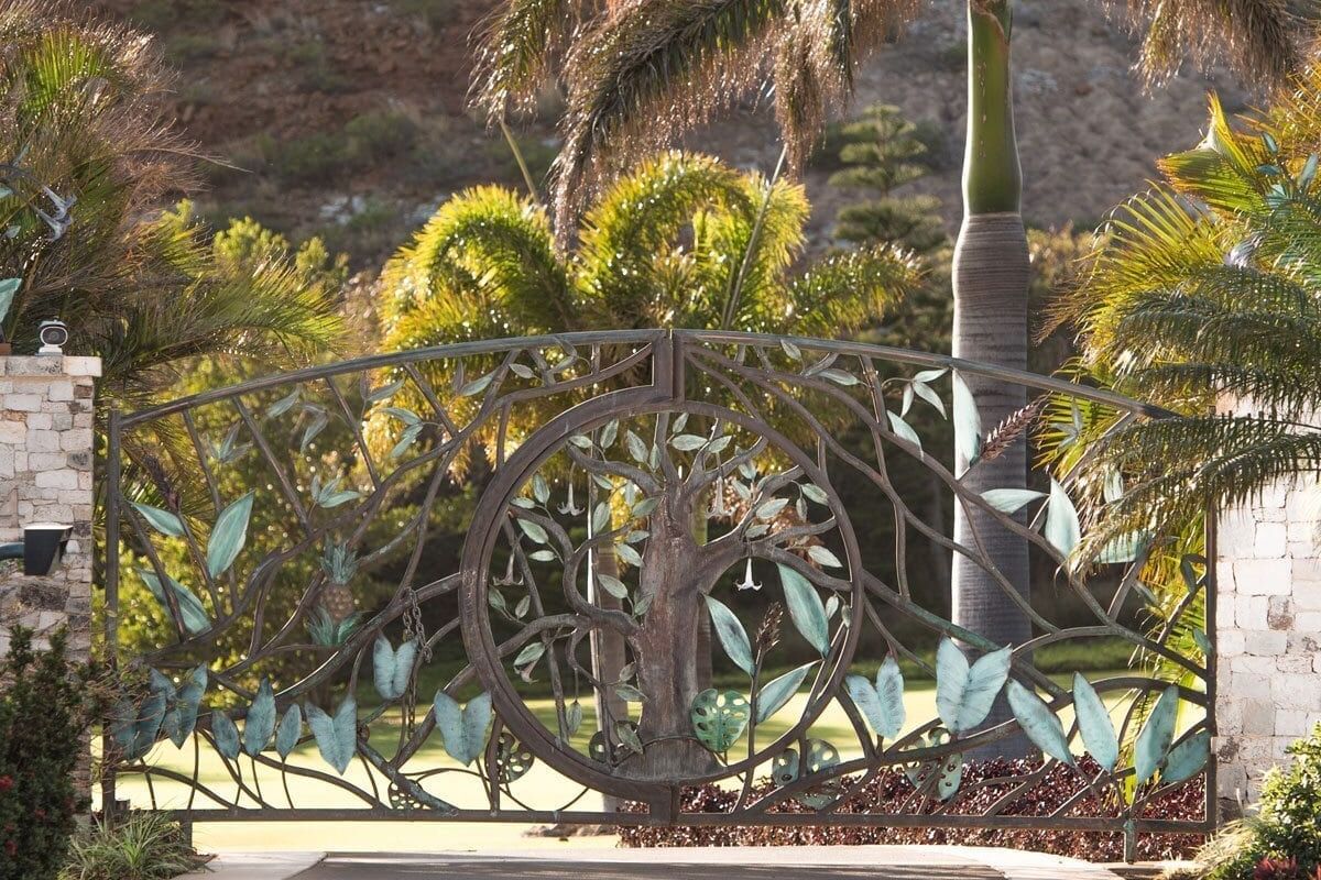 Ornate iron gate with tropical plants behind it.