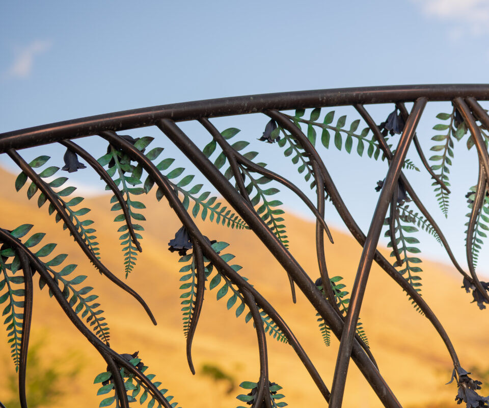 Metal sculpture of ferns against a sunset sky.
