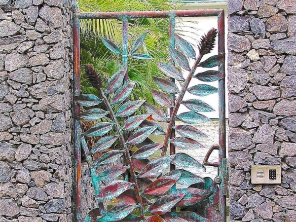 Metal gate with leaf design between stone walls in a garden.