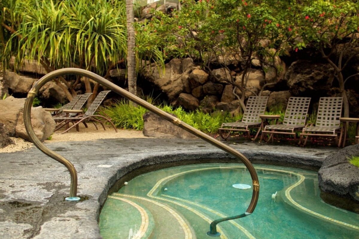A serene hot tub surrounded by greenery and stone seating.