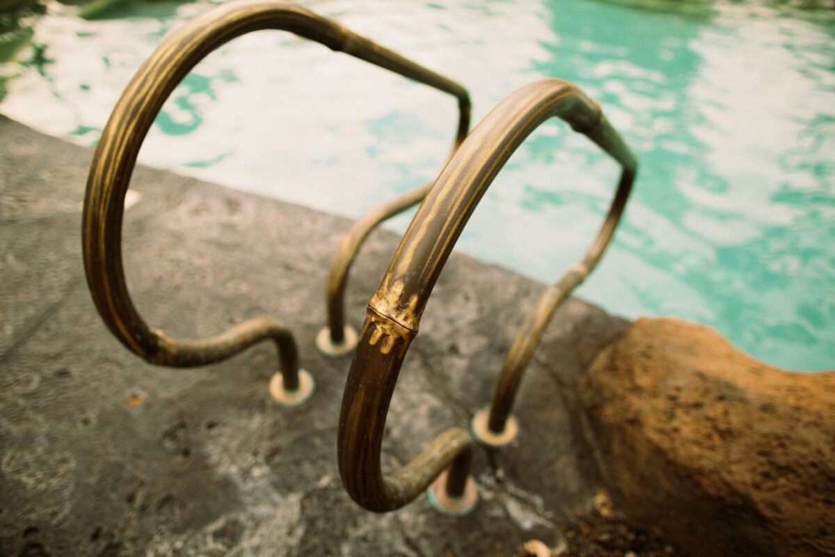 Close-up of a brass pool ladder with water in the background.