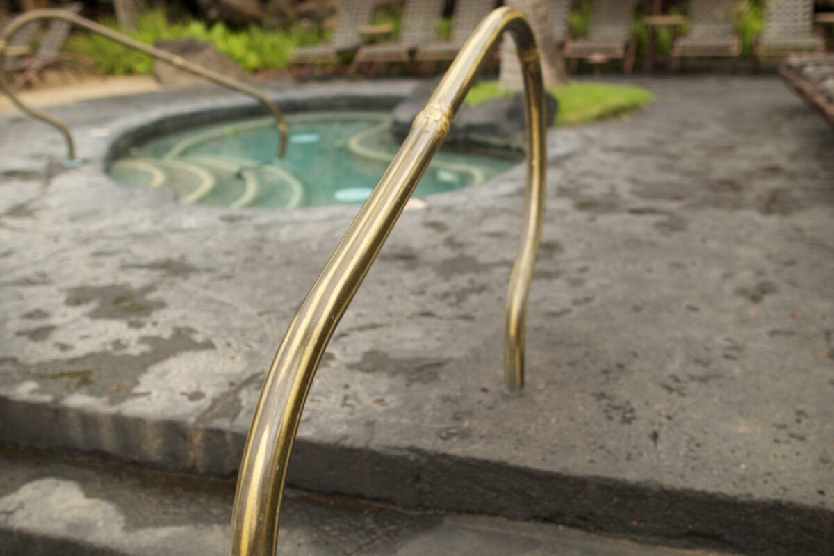A rustic metal handrail leading to a stone hot tub outdoors.