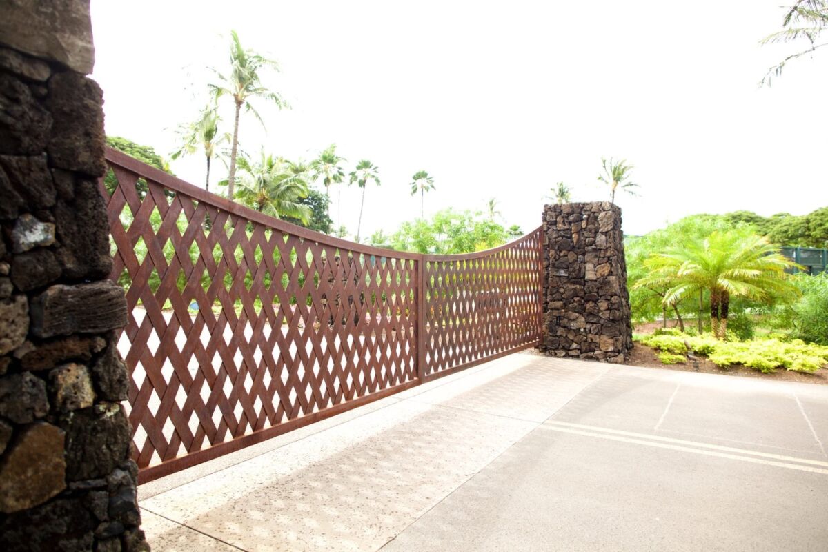 Decorative brown lattice fence with stone pillar in a sunny garden.