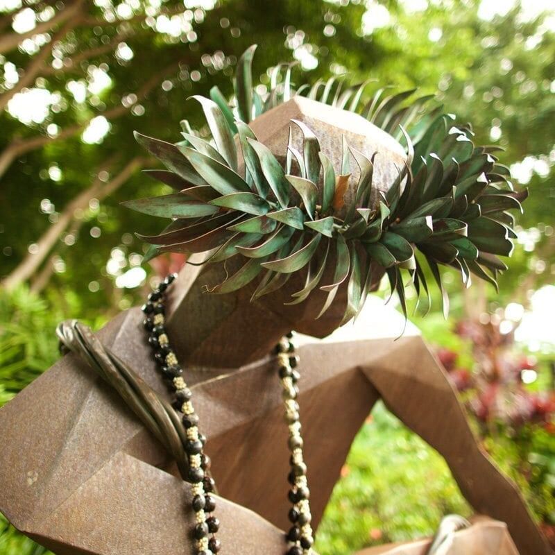 Elderly person adorned with leafy headpiece and traditional beads.