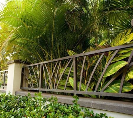 Decorative metal fence with tropical plants in the background.