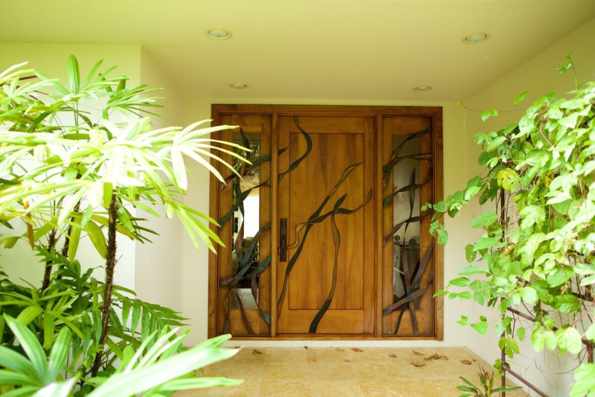 Decorative wooden double doors with artistic metalwork and surrounding greenery.