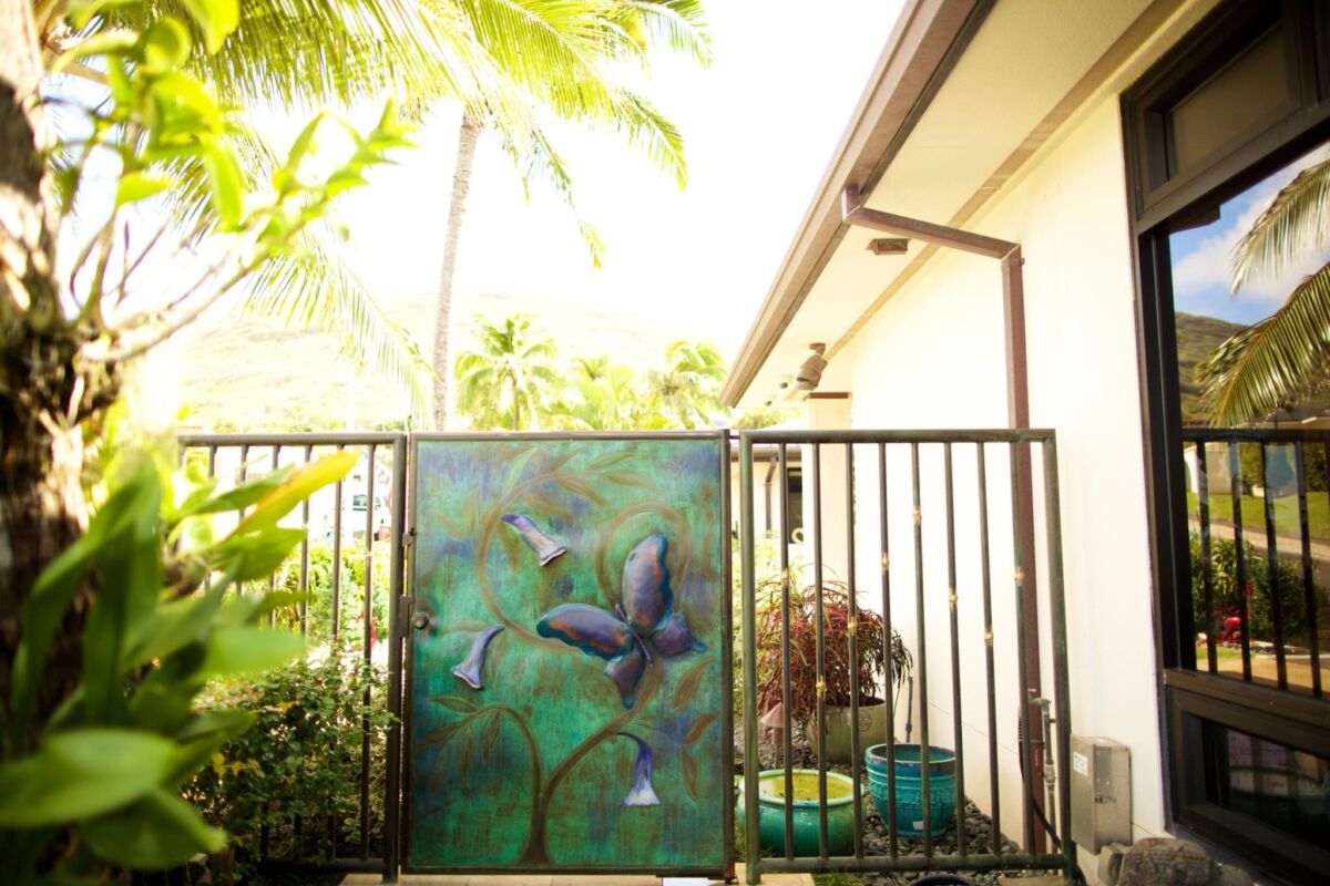 A decorative butterfly painting on a fence with tropical plants in the background.