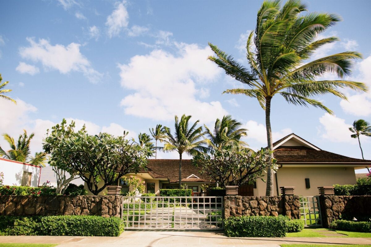 A tropical house with palm trees under a blue sky.