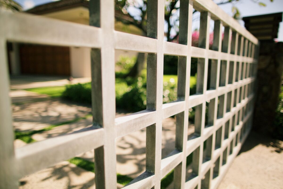 Close-up of a white grid-patterned fence with blurred greenery behind it.