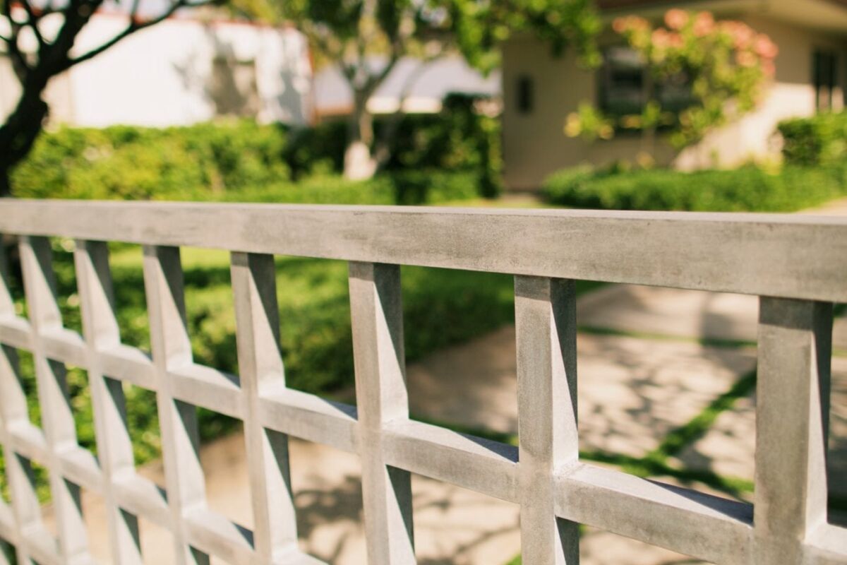 Close-up of a white metal fence with a blurred house and trees in the background.