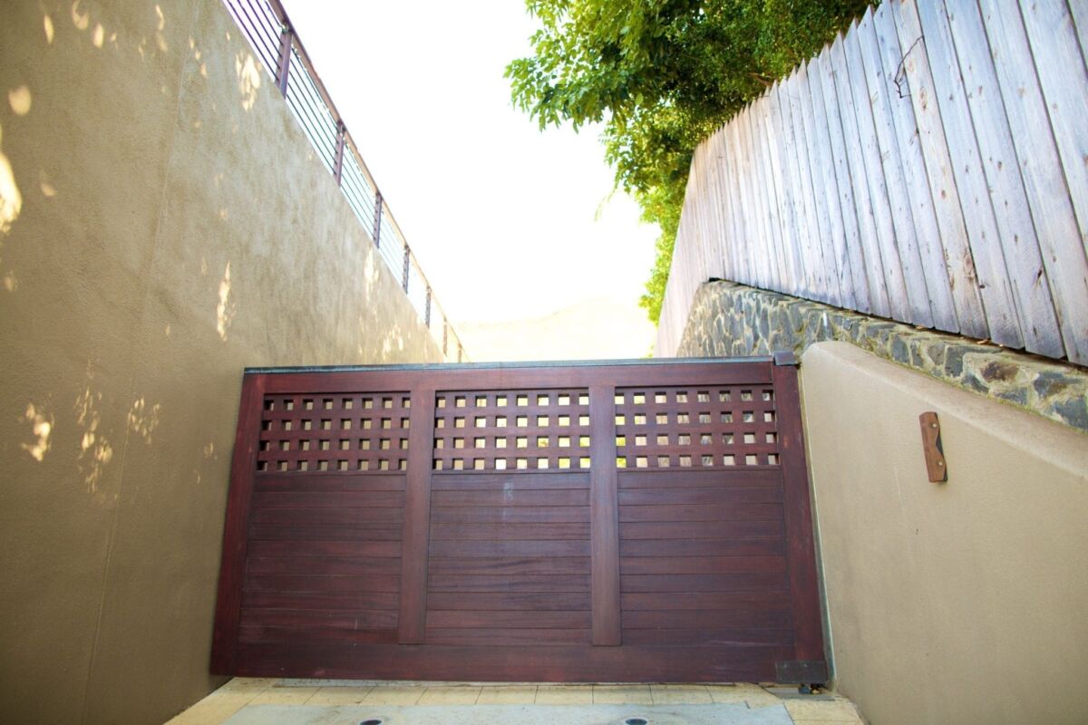 A brown wooden gate with perforated panels in a narrow passageway.