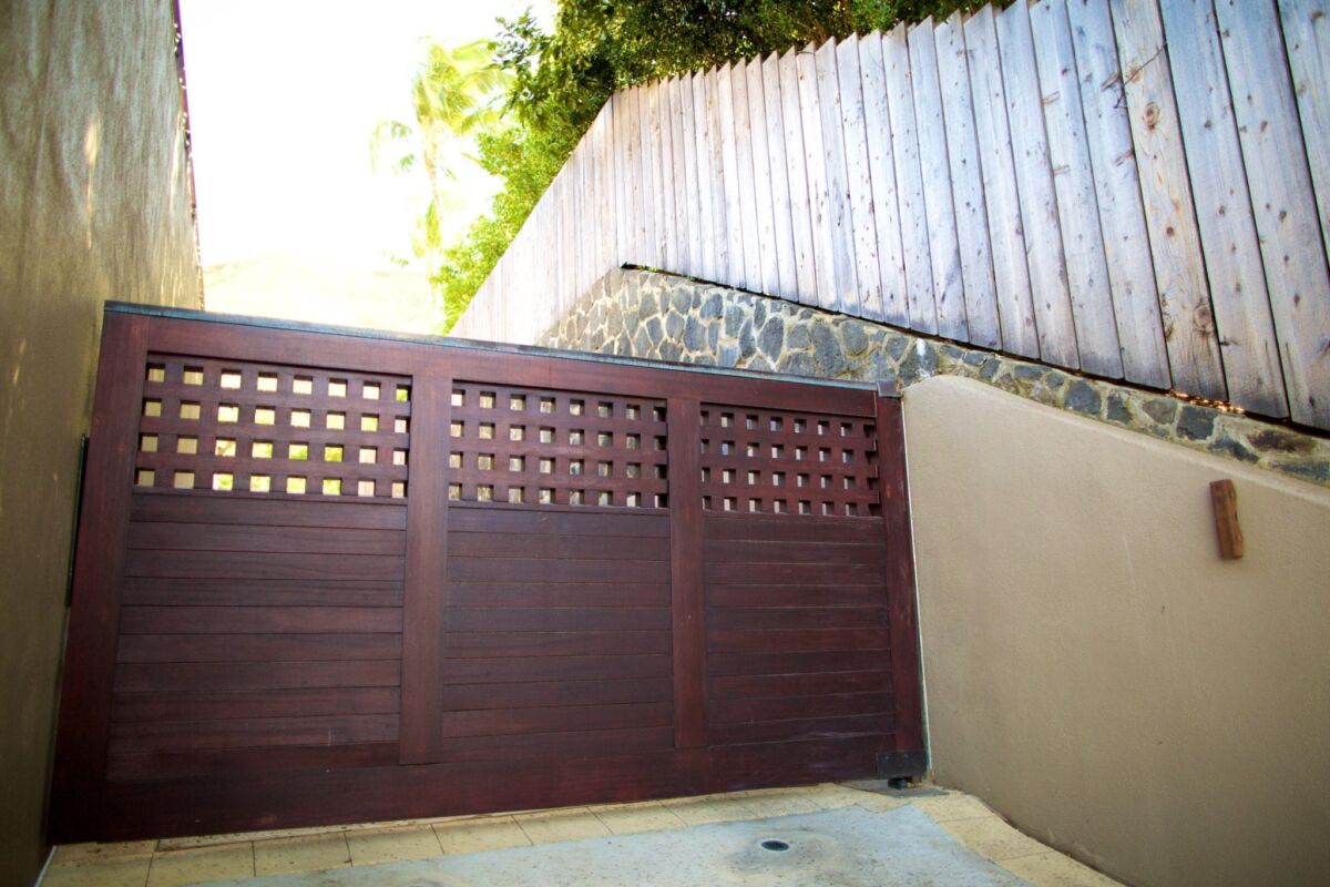 A wooden gate with lattice design next to a tall fence and stone wall.