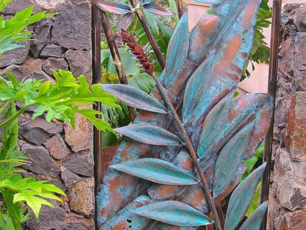 Rustic metal leaf sculpture mounted on a stone wall with green foliage.