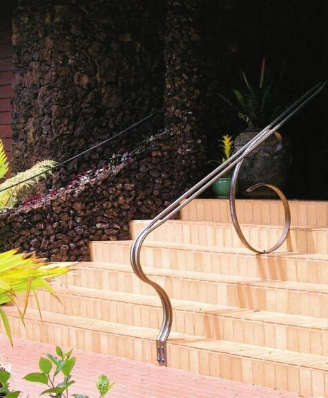 A curved metal handrail along outdoor stone steps with plants nearby.