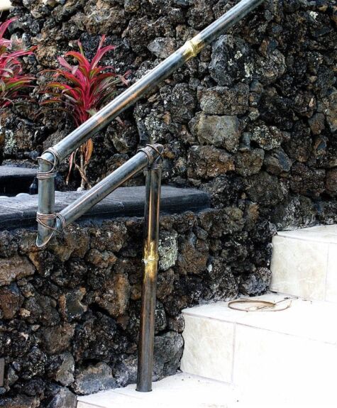 White stone staircase with metal railing beside a dark textured stone wall and red plants.