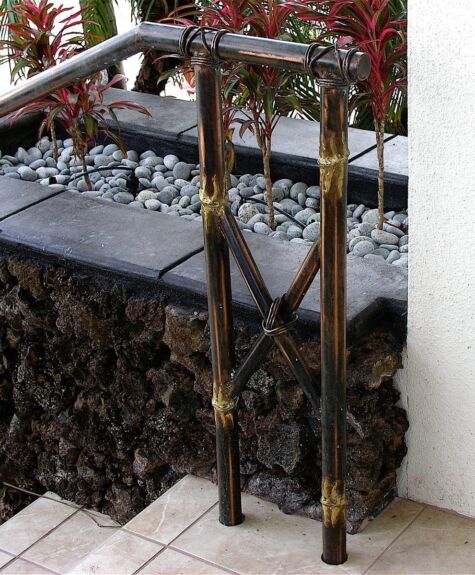 A rustic outdoor faucet with two spouts and a garden hose attached.