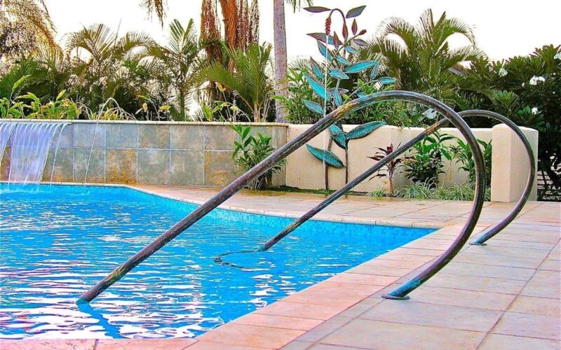 A swimming pool with metal handrails and surrounding plants.