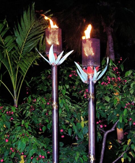 Two flaming tiki torches glowing at night in a garden.