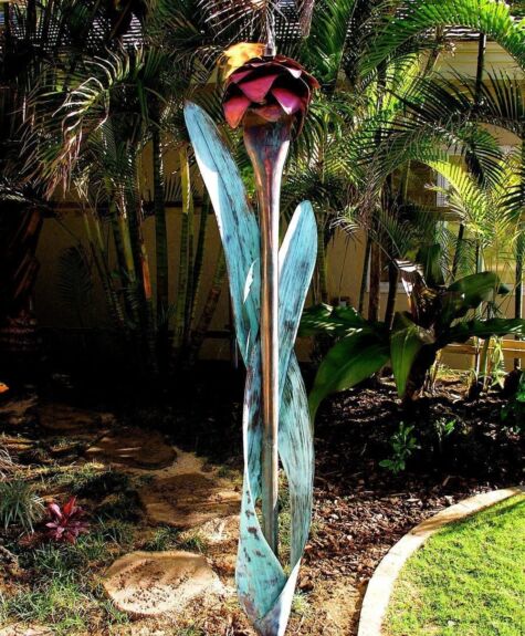 Tall blue glass sculpture resembling leaves in a garden at night.