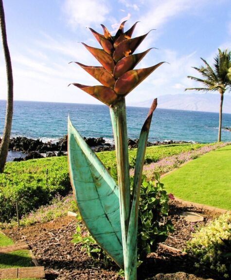 A metal sculpture of a flower with the ocean in the background.