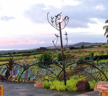 Metal sculpture of a bird in a garden with scenic background.