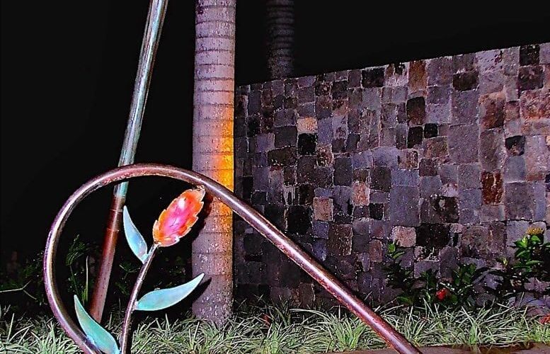 Decorative metal sculpture of a flower near a brick wall at night.