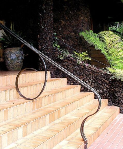Curved metal handrail alongside outdoor steps with greenery.
