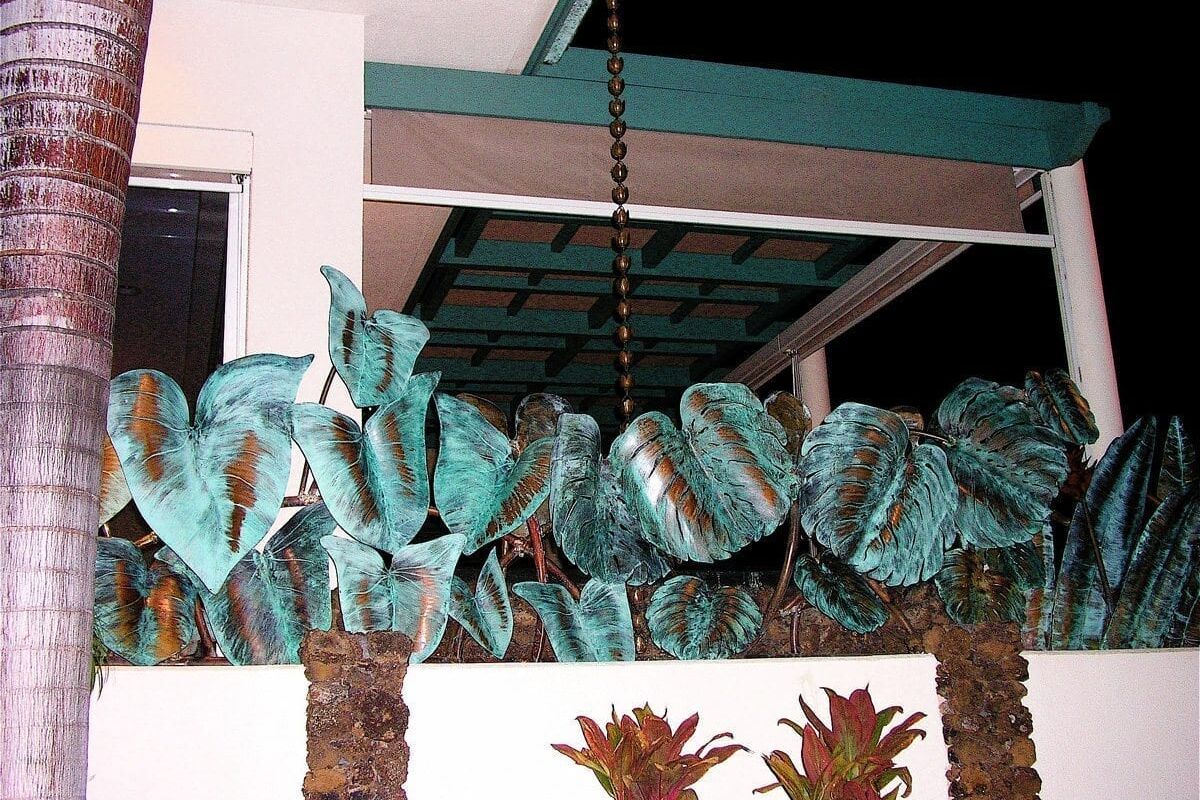 Tall palm trees with large blue-green leaves behind a white fence at night.