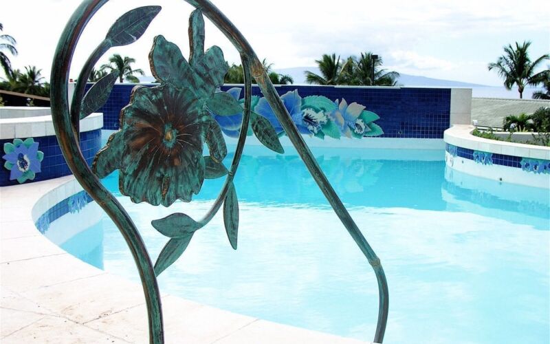 Decorative metal sunflower railing by a clear swimming pool.
