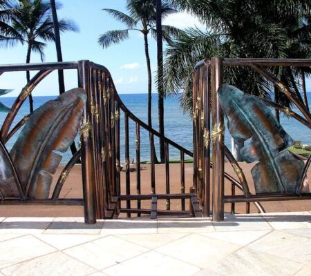 Decorative gate with dolphin sculptures overlooking a beach and ocean.